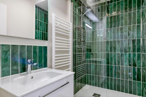 La salle de bains est pourvue d'un lavabo et de murs carrelés verts. dans l'établissement Le Dauphin, à Pornichet