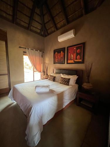 a bedroom with a large white bed with a window at Pumula Bush Chalet in Mabula