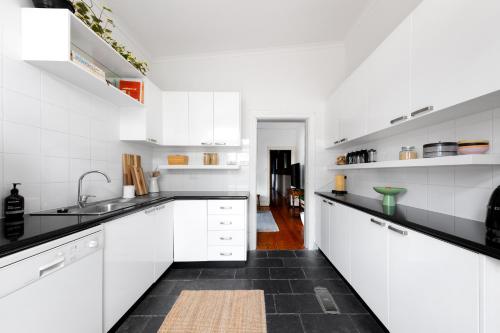 a kitchen with white cabinets and black counter tops at Iconic Lygon street Home, Carlton in Melbourne