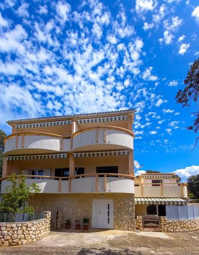 a building in front of a blue sky with clouds at Apartments MULOBEDANJ in Lun