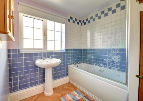 a blue tiled bathroom with a sink and a bath tub at Crossing Keepers Cottage in Grosmont