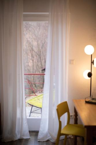 a window with white curtains and a table and a chair at DAS SCHÖNE LEBEN Pop-Up Hotel in Hornberg