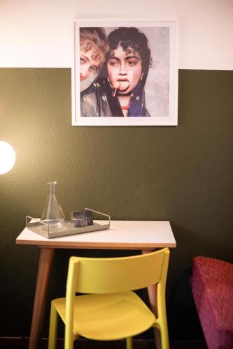 a table with a yellow chair and a picture on the wall at DAS SCHÖNE LEBEN Pop-Up Hotel in Hornberg