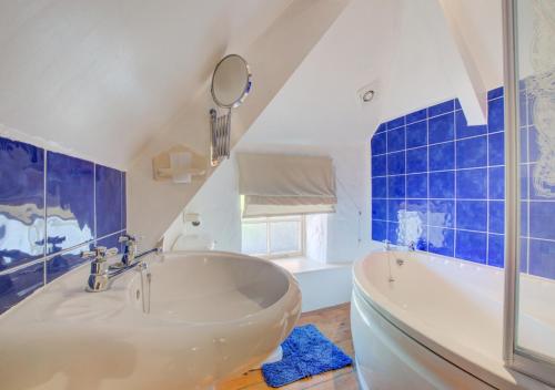 a bathroom with a tub and a mirror and blue tiles at Renes Cottage in Ruan Minor