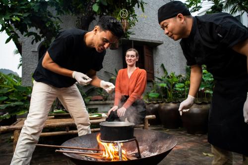 two men and a woman cooking over a grill at Nham Village Resort in Ninh Binh