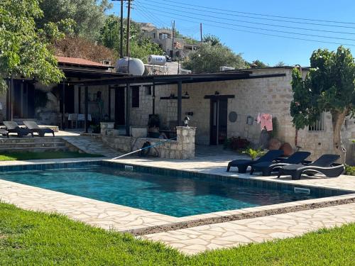 una piscina con dos personas sentadas en sillas junto a una casa en Romanos Villa, en Pafos