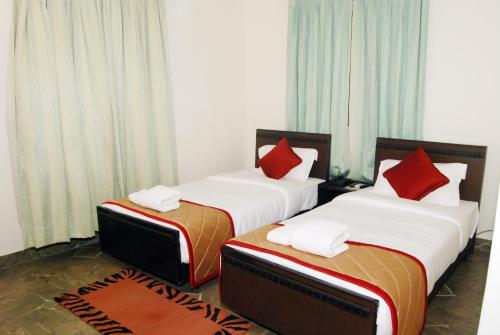 two beds with red pillows in a room at The Altruist Business Stays, Manayata Tech Park in Bengaluru