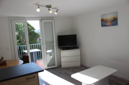 a living room with a television and a balcony at La petite Rascasse, Appartement avec Terrasse ensoleillée in Rayol-Canadel-sur-Mer