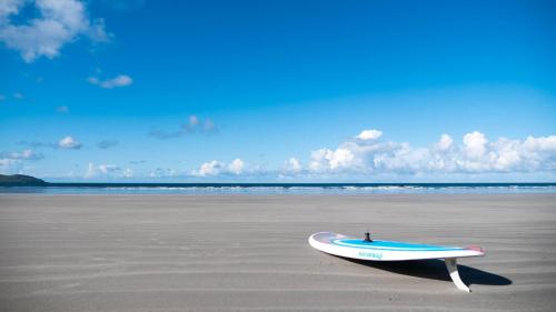 a surfboard sitting on the sand on a beach at Luxurious 5 bedroomed home with sea view close to beach in Lettermacaward