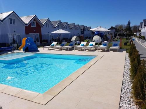 a swimming pool with chairs and umbrellas at a resort at Zatoka Slonca - Domki z basenem, WiFi i parking w cenie! in Mielno