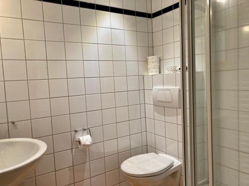 ヴァンガーオーゲにあるHaus Fregatte Whg 1の白いタイル張りのバスルーム(トイレ、シンク付)
