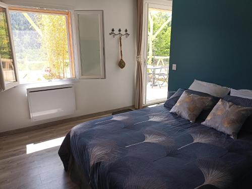 a bedroom with a bed with a blue comforter and windows at instant de tranquillité en Cévennes in Aujac