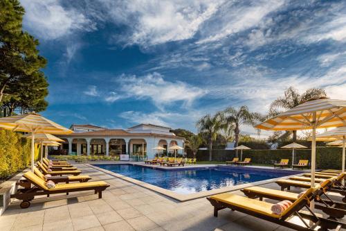 a swimming pool with lounge chairs and umbrellas at The Magnolia Hotel in Quinta do Lago