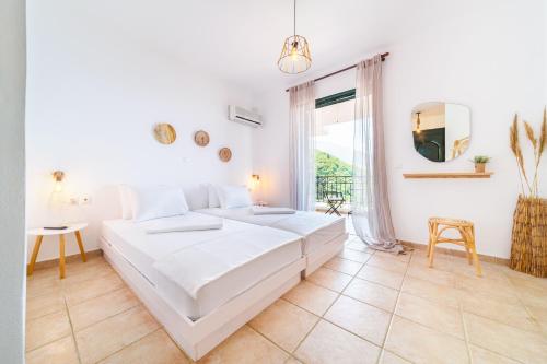 a white bedroom with a large bed and a window at Giannatos Studios- Isabella in Poros