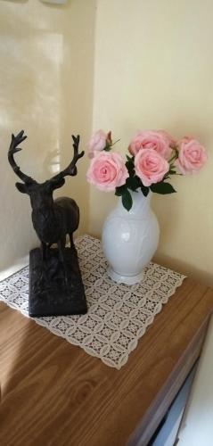 a table with a vase and a statue of a deer and pink roses at Dame vam pokoj - 4 pokoje se sdilenou kuchyni, kapacita max 9 osob in Harrachov