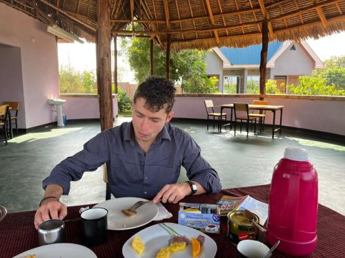 Kili View Lodge في موشي: رجل يجلس على طاولة مع طبق من الطعام