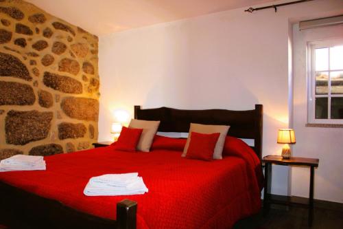um quarto com uma cama vermelha e uma parede de pedra em Casa da Cuca em Campo do Gerês