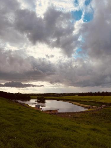 a river in a field with a cloudy sky at East Learmouth Lakeside Lodges - Larch Lodge in Cornhill-on-tweed