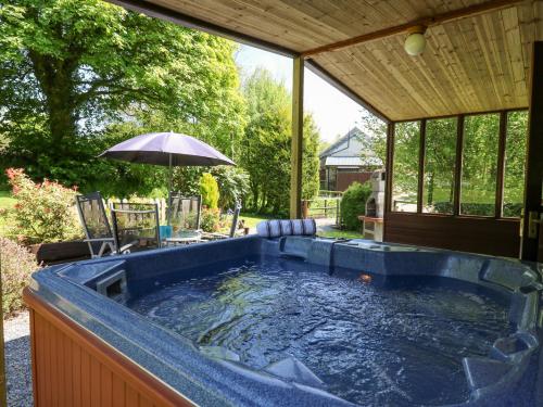 a hot tub in a backyard with an umbrella at Brook Lodge in Llandysul