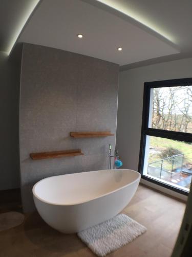 une grande baignoire blanche dans une salle de bain avec une fenêtre dans l'établissement la villa du Lys Toulouse Occitanie Piscine & golf, à Seilh