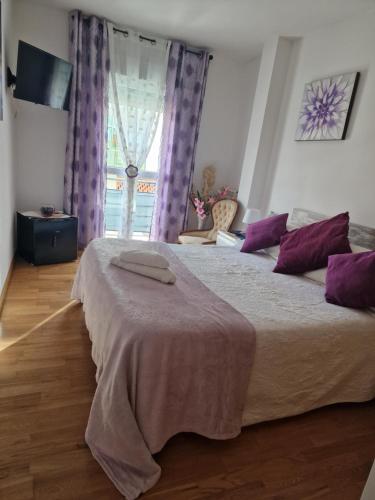a bedroom with a bed with purple pillows and a window at Pension Myriam O PEDROUZO in O Pedrouzo