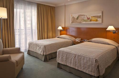 a hotel room with two beds and a chair at Bourbon Residence Barra da Tijuca - Rio de Janeiro in Rio de Janeiro