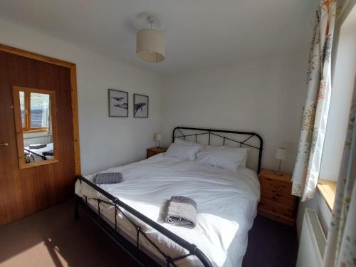 a bedroom with a bed with white sheets and a window at Ocean Surf in Clashnessie