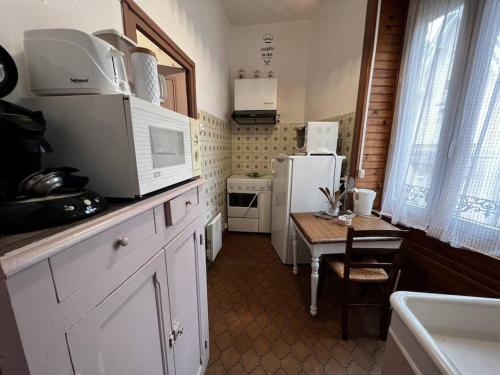 une cuisine avec une table et un réfrigérateur blanc dans l'établissement Le nid douillet Rustique Linge fourni, à La Bourboule