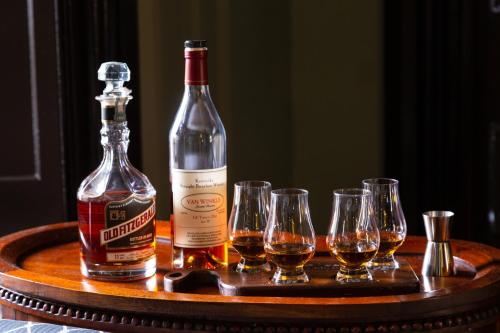 a bottle of whiskey and four wine glasses on a table at Inn at Woodhaven-In the Heart of the Bourbon Trail-Over 12 Distilleries Nearby in Louisville