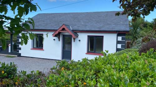 a white cottage with a black door and red windows at Hill Sea View Cottage in Glengarriff