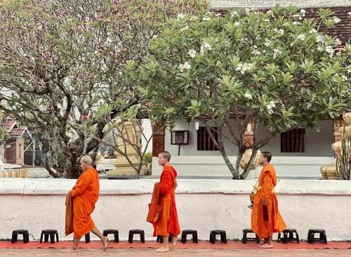 Tres monjes caminando delante de un edificio en Barn Laos Luangprabang Hostel, en Luang Prabang