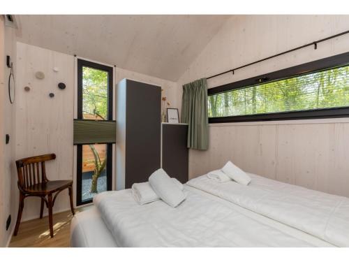 1 dormitorio con 2 camas, silla y ventanas en Enjoy a holiday in the cozy Tiny house on the edge of the forest and the dunes!, en Zoutelande