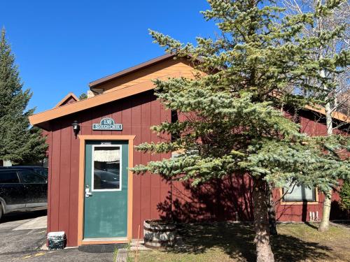 a red building with a green door next to a tree at Faithful Street Inn in West Yellowstone