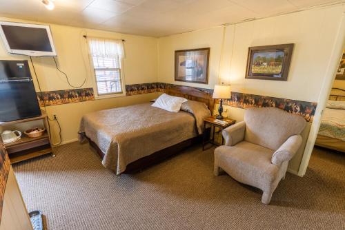 um quarto com uma cama, uma cadeira e uma televisão em Sunset RV Park and Motel em Belle Fourche