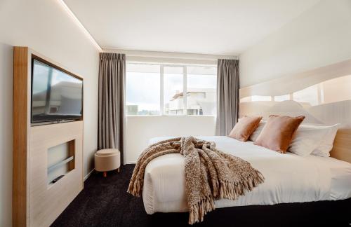 a bedroom with a large bed with a tv and windows at CitySide Hotel Tauranga in Tauranga