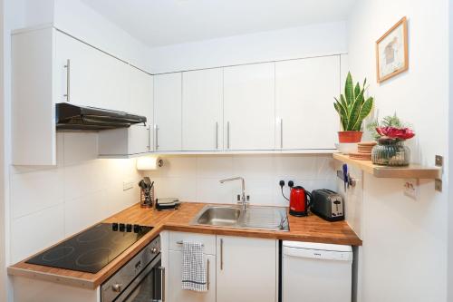 a kitchen with white cabinets and a sink at Bright 2-bed garden flat with skylights in Chelsea in London
