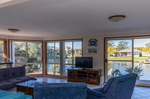 a living room with a couch and a tv and windows at Fishermans Delight Waterfront in Sussex inlet