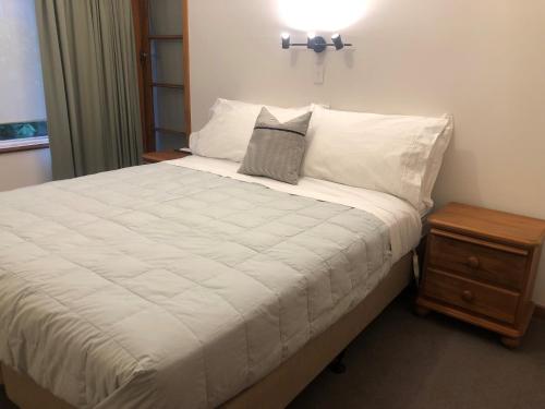 a bedroom with a white bed with a night stand at Seaview Cottage in Oamaru