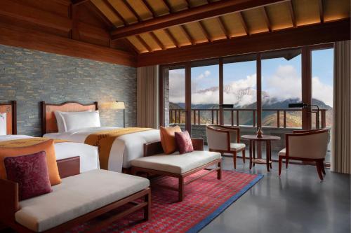 a bedroom with a bed and chairs and windows at Rissai Valley, a Ritz-Carlton Reserve in Jiuzhaigou