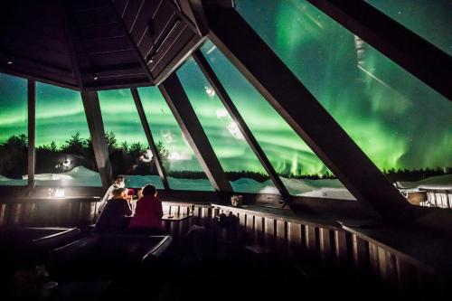a group of people sitting in a building watching the northern lights at Arctic SnowHotel & Glass Igloos in Sinettä