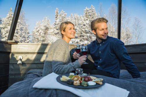 a man and woman sitting on a bed with a plate of food at Arctic SnowHotel & Glass Igloos in Sinettä