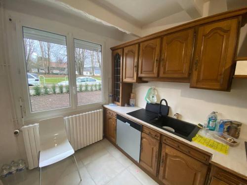 une cuisine avec des armoires en bois, un évier et une fenêtre dans l'établissement Charmante maison au coeur de la nature, à Cany-Barville