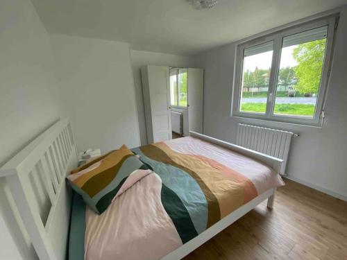 un lit blanc dans une chambre avec une fenêtre dans l'établissement Charmante maison au coeur de la nature, à Cany-Barville