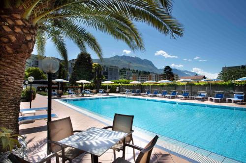 a swimming pool with chairs and a palm tree at SunLake Hotel in Riva del Garda