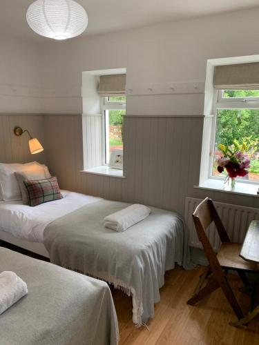a bedroom with two beds and a desk and two windows at The Old Dairy at Walkmill Farm in Bushmills
