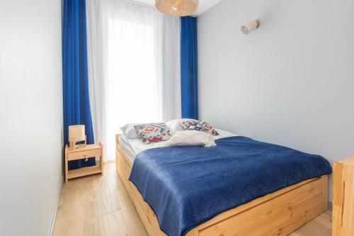 sypialnia z łóżkiem z niebieską pościelą i oknem w obiekcie Apartamenty Mierzeja NCNK Baltic Garden Sztutowo w Sztutowie