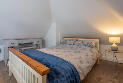 a bedroom with a bed with a blue blanket and a desk at Beau View Cottage in Bekesbourne