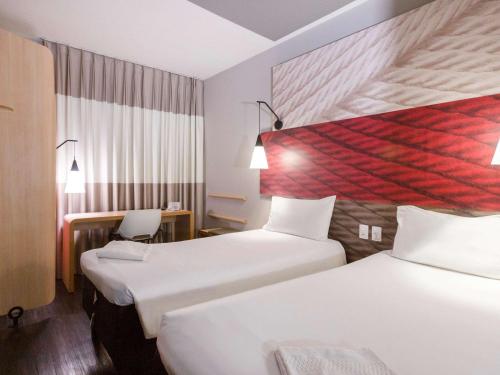 um quarto de hotel com duas camas e uma secretária em ibis Santos Gonzaga Praia em Santos