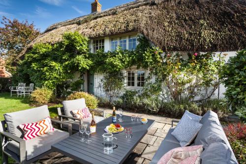a thatched cottage with a table and chairs at Wisteria Cottage in Urchfont