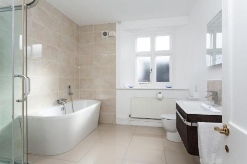 a white bathroom with a tub and a toilet at Solebay Cottage in Lower Boscaswell